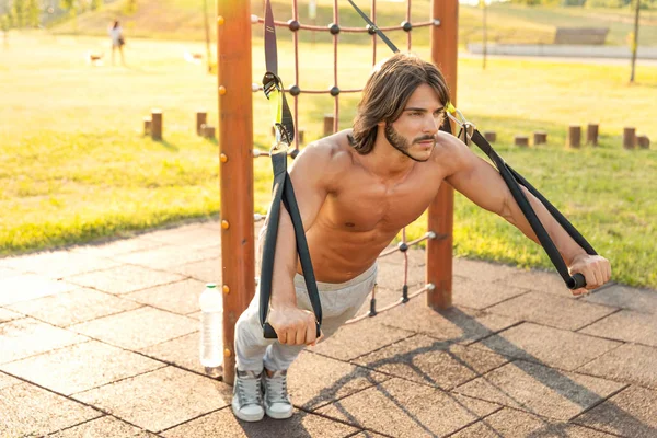 여름의 화창한 피트니스 공원에서 서스펜션 트레이너와 극단적 운동하는 심각한 남자결정 — 스톡 사진