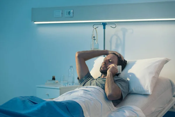夜遅く 病院のベッドに横になり フォンに話している大人の男性患者を心配痛みで — ストック写真