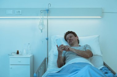 Uykusuz endişeli hasta gece geç saatte hastanede yatıp akıllı telefonuyla sohbet ediyor.