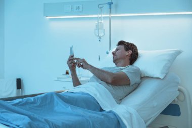 Uykusuz endişeli hasta gece geç saatte hastanede yatıp akıllı telefonuyla sohbet ediyor.