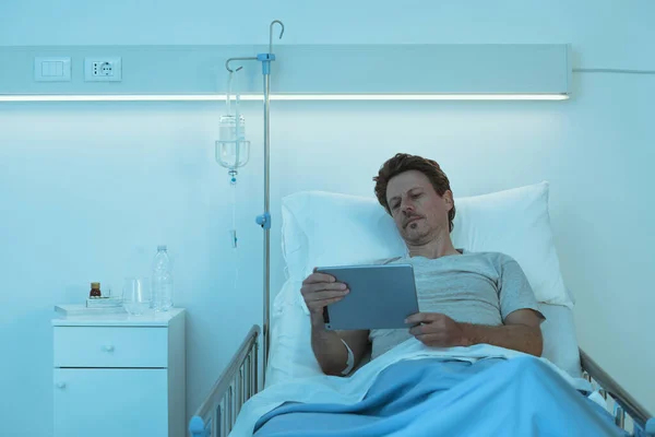 大人の眠れない患者は夜に病院のベッドに横たわって 彼は彼のデジタルタブレットで映画を見ています — ストック写真