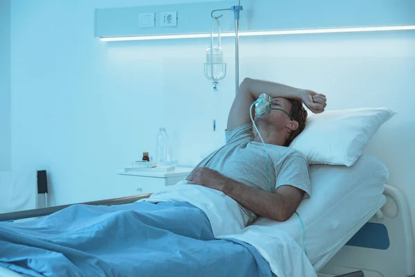 夜に病院のベッドに寝そべって酸素マスクをしている大人の男 — ストック写真