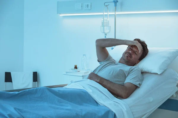 夜に病院のベッドに寝そべっている大人の男が苦しんでいる — ストック写真