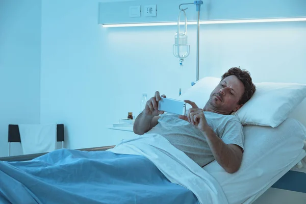 침대에 이루는 환자는 스마트폰으로 비디오를 — 스톡 사진