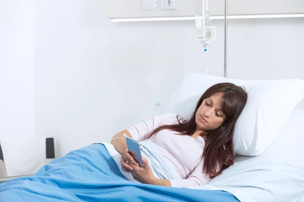 寝たきりの女性患者が病院のベッドに横になってスマホとおしゃべりをしていた — ストック写真