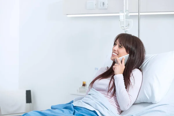 病院のベッドに横になって電話で話している若い女性患者の笑顔 — ストック写真