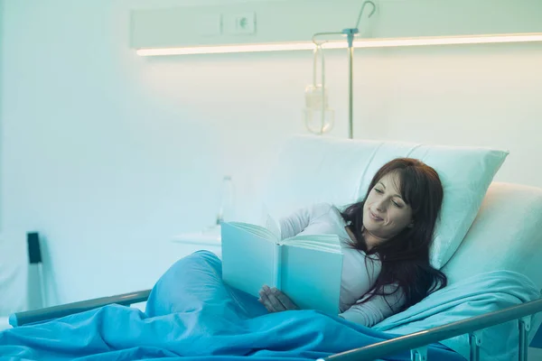 夜に病院のベッドに横になって本を読んでいる若い女性 — ストック写真