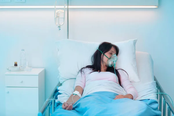 Young woman lying in a hospital bed at night and she is sleeping and wearing an oxygen mask