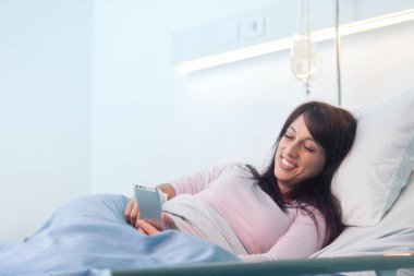 Uykusuz kadın hasta hastanede uzanıyor ve akıllı telefonuyla sohbet ediyor.