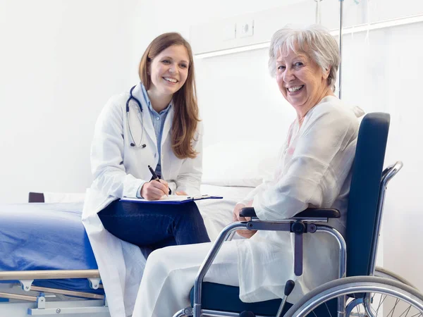 看護師又は医師が 車椅子に座っている笑顔の高齢者の女性のために病棟に患者ノートを書きます医療と医療の概念 ロイヤリティフリーのストック画像