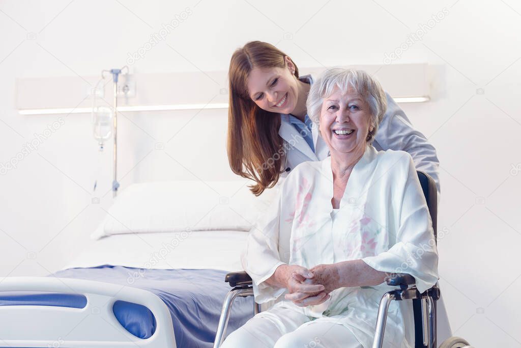 Smiling happy senior woman in a wheelchair in hospital or an old-age home being wheeled by a doctor or nurse during rehabilitation from an injury or surgery