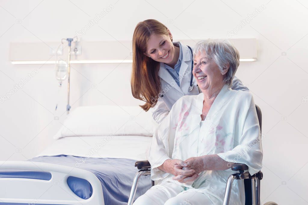 Smiling happy senior woman in a wheelchair in hospital or an old-age home being wheeled by a doctor or nurse during rehabilitation from an injury or surgery