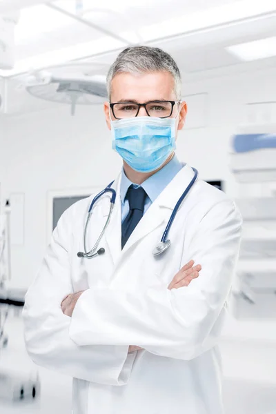 Doctor wearing a surgical mask against infections standing with crossed arms in a lab coat isolated on white in a corona virus or Covid-19 concept