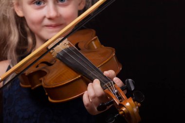 Mutlu küçük sarışın kız keman koyu arka plan üzerinde oynamak