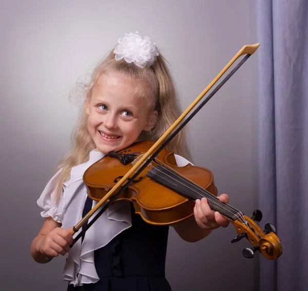Счастливая маленькая девочка играет на скрипке на сером фоне — стоковое фото
