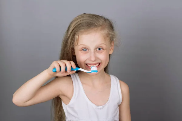 Concetto di stile di vita sano. Prendersi cura dei denti dei bambini. Ragazza lavarsi i denti su sfondo grigio — Foto Stock