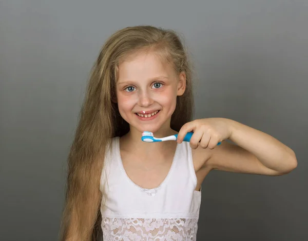 Joyful little girl cleans your teeth on grey background. Portrai — Stock Photo, Image