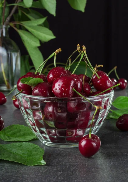 Crystal bowl with cherries in water drops on dark background