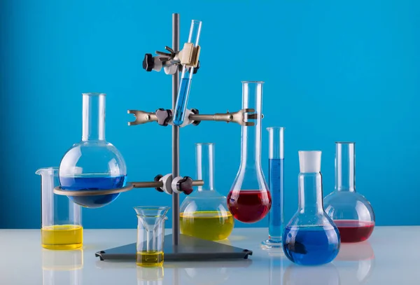 Laboratoire biologique. Un trépied avec une variété de verre chimique et de liquides colorés sur un fond bleu — Photo