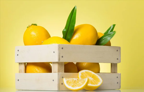 Frische saftige Zitronen in einer Holzkiste auf gelb — Stockfoto