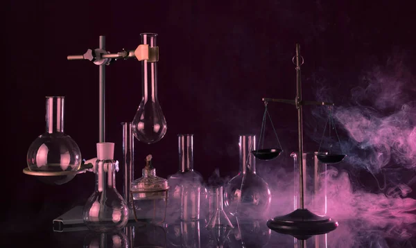 Laboratorio magico. Bilance chimiche, treppiede con varietà di piatti su fondo scuro nel fumo rosso — Foto Stock
