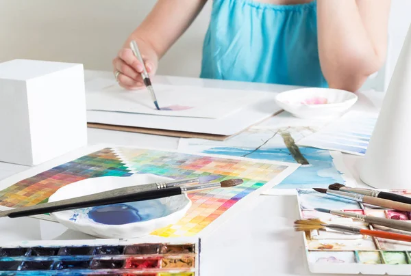 Menina artista pintura imagem com aquarelas na mesa em estúdio brilhante — Fotografia de Stock