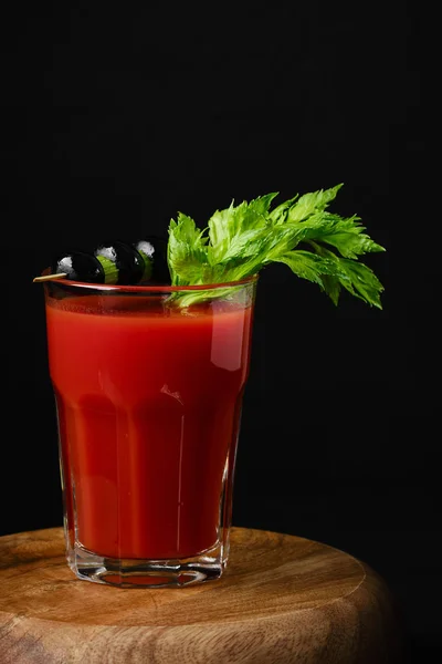 Tomato juice with celery and black olives. black background