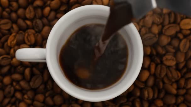 Kaffee, der aus der Geysir-Kaffeemaschine in die Tasse gegossen wird. Kaffeebohnen als Hintergrund. Draufsicht in Zeitlupe