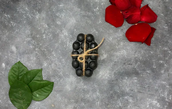 Black charcoal volcanic soap and herbal leaves red rose petals on grey background. Put your text.