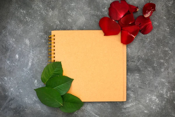 Note book and red rose petals isolated on black grey background. New life concept.