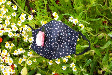 Haşhaş tarlasının arka planında çimlerin üzerinde duran el yapımı pamuk surat maskesi. Coronavirus Covid 19 'a karşı ev yapımı kumaş maske..