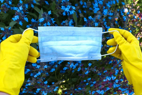 Hand holding cotton face mask at the nature flowers field background. Home made cloth face mask against coronavirus Covid 19.