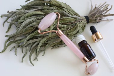Beyaz arka planda kuru otların üzerinde duran pembe yüz silindiri. Güzellik aletleri. Yüz için Quartz silindirli masaj aracı.