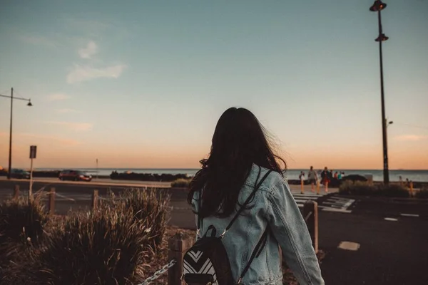 Jovem mulher caminhando na calçada com um céu azul claro e de costas — Fotografia de Stock