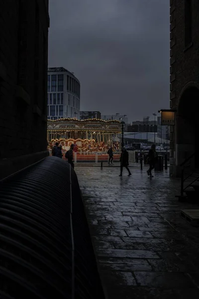 Vertikální záběr skupin lidí procházejících se po kolotoči během deštivého oblačného dne ve městě — Stock fotografie