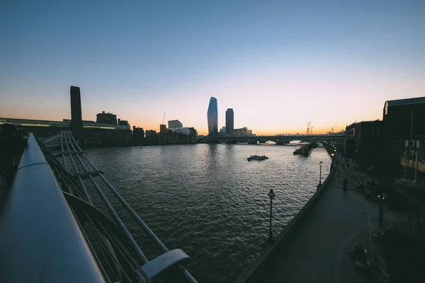 Ponte moderna sobre a água com a construção da cidade na distância ao pôr do sol — Fotografia de Stock