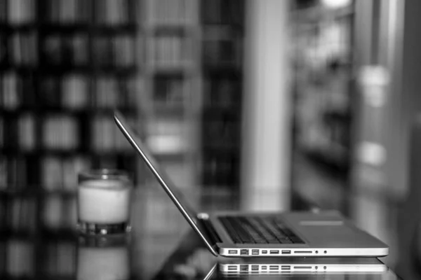 Closeup shot of a laptop on a glass table with blurred background in black and white