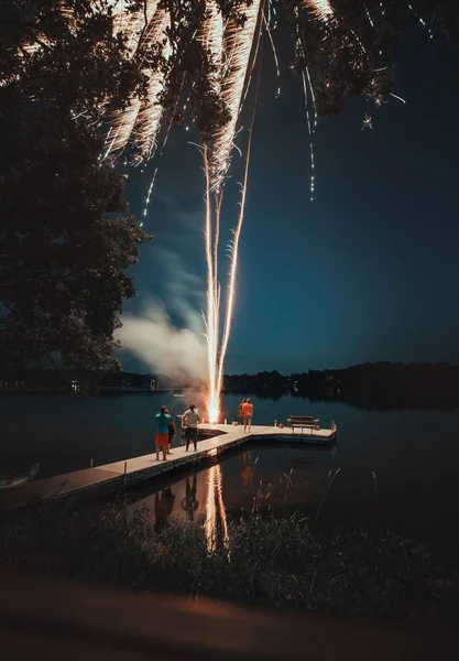 Vertical shot of people standing on a white dock near a lake lighting fireworks during nighttime — Stock Photo, Image
