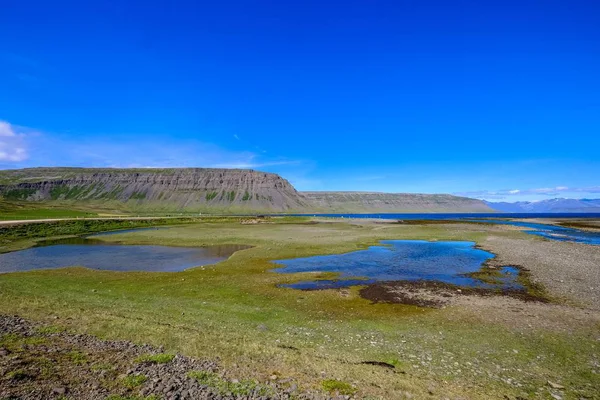 맑고 푸른 하늘 아래 먼 거리의 산과 물 근처의 작은 연못이있는 잔디 밭 — 스톡 사진