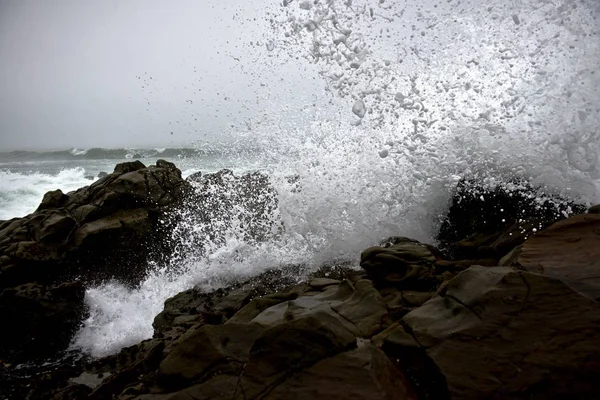 Gyönyörű csobbanás óceán hullámai sziklák alatt egy esős napon — Stock Fotó