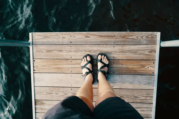 Voeten van een mannetje staan op een houten oppervlak over het waterlichaam — Stockfoto