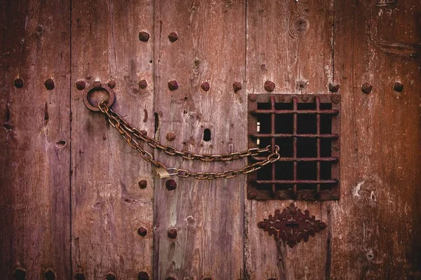 Gros plan d'un vieux cadenas rouillé sur une grande porte en bois avec une petite clôture métallique — Photo