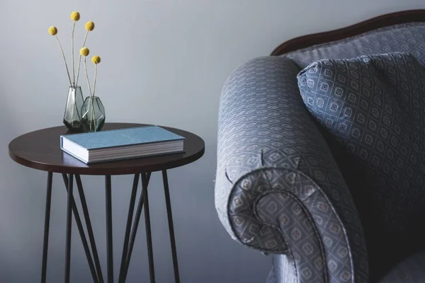 Tiro de un sofá azul cerca de una pequeña mesa redonda con un libro y dos jarrones con plantas amarillas — Foto de Stock