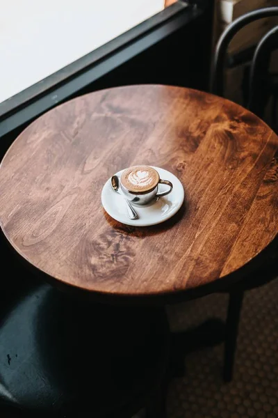 Sehr gut gemachter Cappuccino in einer Tasse mit Blumenkunst auf Schaumstoff auf einem runden Holztisch — Stockfoto