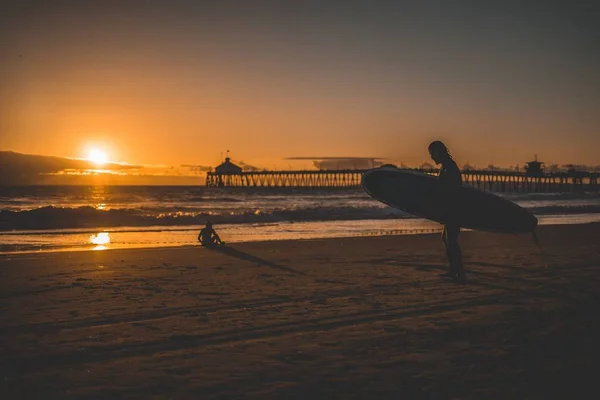 Silhueta de um surfista em uma praia de areia com o pôr do sol no fundo — Fotografia de Stock