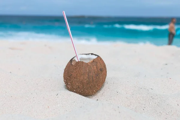 Close-up shot van een bruine kokosnoot met een rietje in het op zand — Stockfoto