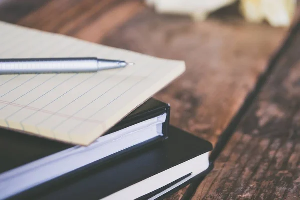 Primer plano de los libros de texto con una pluma gris y pedazos arrugados de papel alrededor de una superficie de madera — Foto de Stock