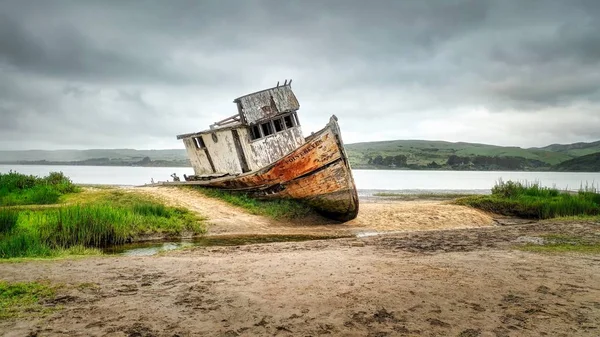 Tiro largo de um navio enferrujado destruído na costa de um lago — Fotografia de Stock