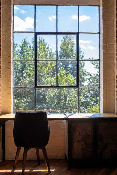 Tiro vertical de uma cadeira e uma mesa perto de uma grande janela com uma vista incrível da vegetação fora Fotos De Bancos De Imagens