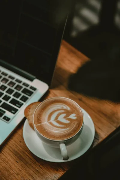 Una taza de café con leche bien hecho junto a una computadora portátil — Foto de Stock